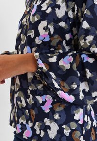 Blusa floreale navy con motivi multicolori in rosa, verde e bianco. Presenta un tessuto testurizzato e maniche arricciate.