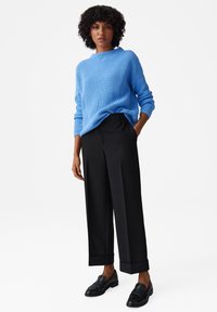 Maglione a coste blu chiaro, pantaloni neri a gamba larga e mocassini neri. Il maglione ha un collo a girocollo; i pantaloni hanno i risvolti.