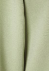 Tessuto verde chiaro con una superficie liscia, caratterizzato da linee sottili e discrete e una finitura uniforme. Il materiale appare morbido e leggermente elastico.