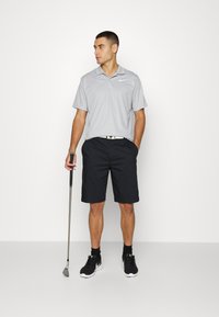 Svetlo siva polo majica s ovratnikom, uparena s crnim šortsem. Outfit je upotpunjen crnim sportskim cipelama i golf palicom.