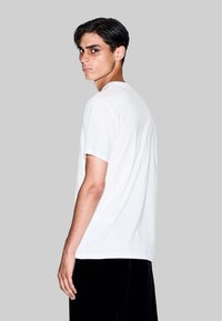 T-shirt bianco in cotone a maniche corte con scollatura rotonda, indossato da un modello maschile. Texture liscia, vestibilità casual, design semplice, senza fantasie.