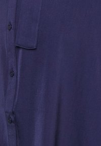 Mörklila skjorta med knappar i smidigt, lätt tyg. Har en bröstficka och sex svarta knappar på framsidan.