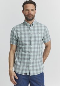 Camicia a maniche corte con bottoni in un motivo a quadri verde chiaro e grigio, dotata di tasca sul petto e un'etichetta tessuta sull'orlo.