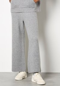 Pantaloni a coste grigio con un fit rilassato, caratterizzati da gambe ampie e una superficie testurizzata. Abbinati a sneakers bianche.