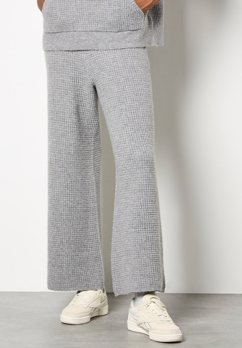 Pantalones de punto en color gris con un corte relajado, que presentan piernas anchas y una superficie texturizada. Combinados con zapatillas blancas.