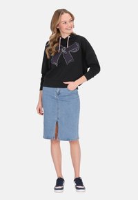 Felpa nera con cordini rosa e grafica a fiocco bianco; gonna a tubino in denim blu con spacco frontale; modella che indossa sneaker navy.
