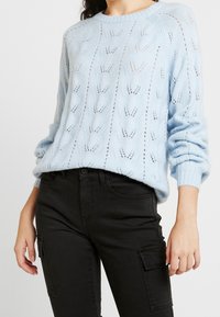 Maglione lavorato a maglia azzurro chiaro con un motivo testurizzato, polsini a coste e vestibilità rilassata, abbinato a jeans cargo neri.