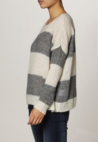 Chunky stickad tröja i krämfärgade och grå ränder, med en avslappnad passform, vid halsringning och ribbad nederkant. Mjuk textur med synliga stygn.