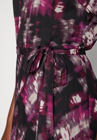 Svart klänning med abstrakta mönster i rosa och vitt, med ett tygbälte knutet i midjan och subtila volangdetaljer på ärmarna.