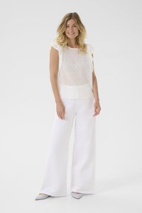 Haut en eyelet blanc avec des manches froncées, assorti à un pantalon large blanc et des chaussures pointues grises claires sur fond uni.