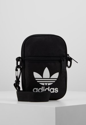 Kleine zwarte Adidas schoudertas met wit trefoil-logo, voorvak met ritssluiting en verstelbare schouderband op een witte ondergrond.