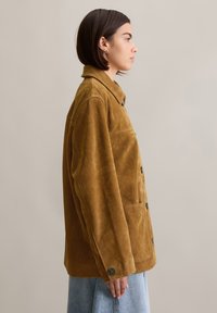 Braune Wildlederjacke mit Kragen, vorderen Knöpfen und Seitentaschen, bietet einen lässigen Schnitt und eine strukturierte Oberfläche.