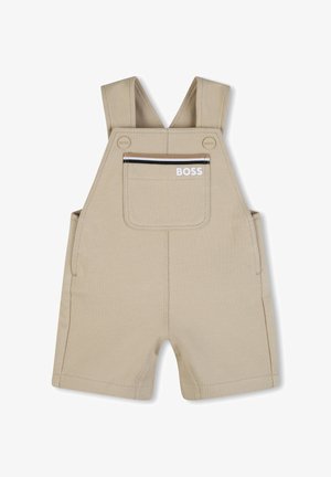 Tuta in cotone beige con spalline regolabili, tasca frontale con cerniera e tasche laterali; presenta un dettaglio con il logo sulla tasca frontale.