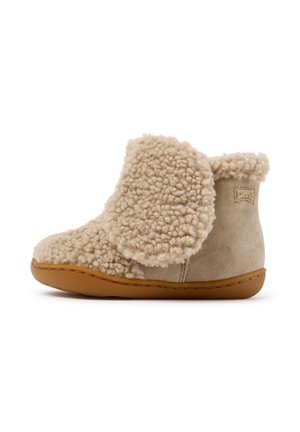 Chausson bottine beige montant jusqu'à la cheville avec extérieur en polaire douce et bouclée, talon en suède et semelle en caoutchouc marron, conçu pour le confort à l'intérieur.