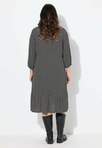 Schwarz-weißer gepunkteter Kleid mit Dreiviertelärmeln und ausgestellt Saum, kombiniert mit kniehohen schwarzen Stiefeln. Glatte Stofftextur.