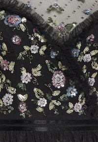 Tissu noir transparent orné de sequins et perles floraux pastel, avec une bordure en dentelle froncée le long de l'encolure et de la taille.