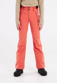 Pantaloni da neve corallo brillante con vita aderente, due tasche cargo laterali e orli rinforzati, abbinati a stivali da neve con punta nera.