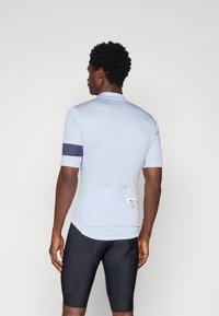 Tricou de ciclism albastru deschis, cu mâneci scurte, buzunar posterior și o dunga bleumarin pe brațul stâng. Purtați cu pantaloni scurți de ciclism negri.
