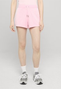Shorts roses en matériau doux, avec une taille à cordon de serrage et une coupe décontractée, assortis à des baskets grises et des chaussettes montantes blanches.