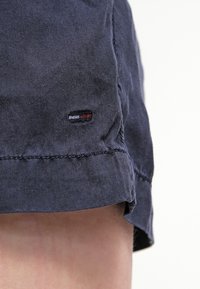 Gros plan sur un short en tissu bleu marine avec un petit logo de marque cousu près de l'ourlet sur la jambe d'une personne.