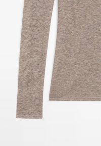 Top a maniche lunghe, aderente, in morbido tessuto a maglia grigio-marrone chiaro. Presenta maniche dritte e un orlo arrotondato, con cuciture piatte per una finitura liscia.