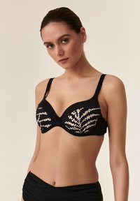 Črn bikini zgornji del s pisanimi, golimi okraski, ki spominjajo na listje praproti; ima nastavljive naramnice in strukturiran dizajn skodelice.