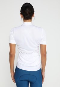 Jersey de ciclismo blanco de manga corta con un diseño ajustado. Presenta un cuello con cremallera y tejido elástico, combinado con pantalones cortos de ciclismo acolchados en azul.