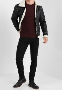 Czarna kurtka z sztucznej skóry z białym kołnierzem z owczej skóry, zestawiona z bordowym swetrem i czarnymi jeansami slim-fit. Posiada zamek błyskawiczny i detale ze stębnowania.
