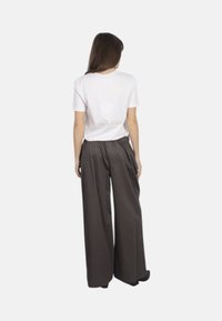 T-shirt blanc et pantalon ample, haut à taille marron foncé. Le pantalon présente une taille élastique et des jambes larges et droites.