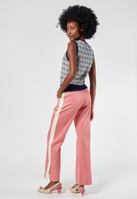 Sleeveless patterned top in navy and cream, paired with pink wide-leg pants featuring white side stripes, and light-colored heeled shoes.