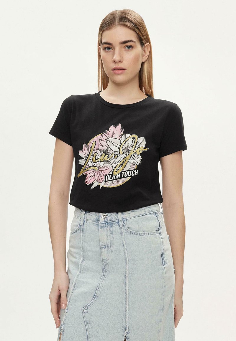 T-shirt in cotone nero con maniche corte, caratterizzato da una stampa grafica floreale in rosa e bianco, e testo decorativo "Glam Touch" in argento.