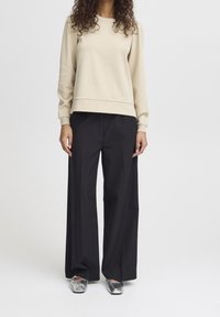 Ljusbeige sweatshirt med långa ärmar, rund hals och ribbade muddar, i kombination med svarta vida byxor och metalliska silverfärgad slip-on skor.