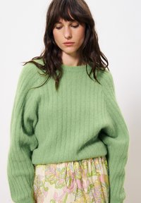 Groene geribde trui van zacht materiaal, met een ronde hals en een relaxte pasvorm, gecombineerd met een rok met bloemenpatroon.