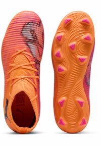 Scarpe da calcio di un vivace arancione con accenti rosa, tomaia testurizzata e suola flessibile con piccoli tacchetti rosa per la trazione.