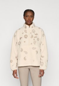 Κρέμ φλις πουλόβερ με ψηλό γιακά, διακοσμημένο με κεντημένα μοτίβα paisley και μισό φερμουάρ μπροστά. Μαλακή υφή, υπερ�μεγέθης εφαρμογή.