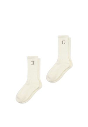 Chaussettes blanches à côtes, fabriquées dans un matériau doux, avec un subtil « II » en gris au niveau de la cheville. Conçues pour le confort et un port quotidien.