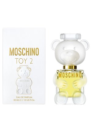 Flacon de parfum Moschino Toy 2 en forme d'ours translucide tenant un liquide jaune, à côté d'une boîte blanche avec du texte doré.