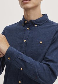 Marineblå knapp-up skjorte i teksturert stoff; har treknapper, en brystlomme og en klassisk kragedesign.