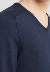 Pull encolure en V bleu marine avec texture côtelée et manches ajustées, fabriqué en matériau doux et léger avec une finition lisse.