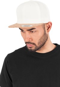 Fehér snapback sapka parafa vízszintes részel. Sima anyag a testén, kontrasztos textúra a vízszintes részen. Alatta egy alap fekete póló van.