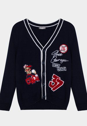 Cardigan bleu marine avec bordure blanche contrastante, fermeture à boutons, et patches brodés représentant un entraîneur, du texte, et le numéro 37.