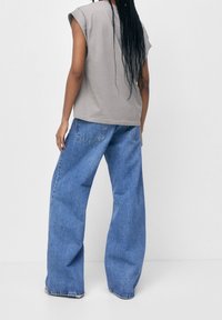 Grå oversized t-shirt med korte ærmer, parret med løse blå denim jeans. Stoffet ser blødt ud med synlige lommer og stikninger.