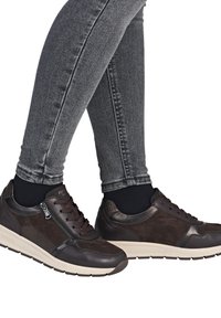 Braune Leder- und Wildledersneaker mit einer weißen Sohle, ausgestattet mit einem seitlichen Reißverschluss, Schnürsenkeln und strukturierten Akzenten. Getragen mit grauen Skinny Jeans.
