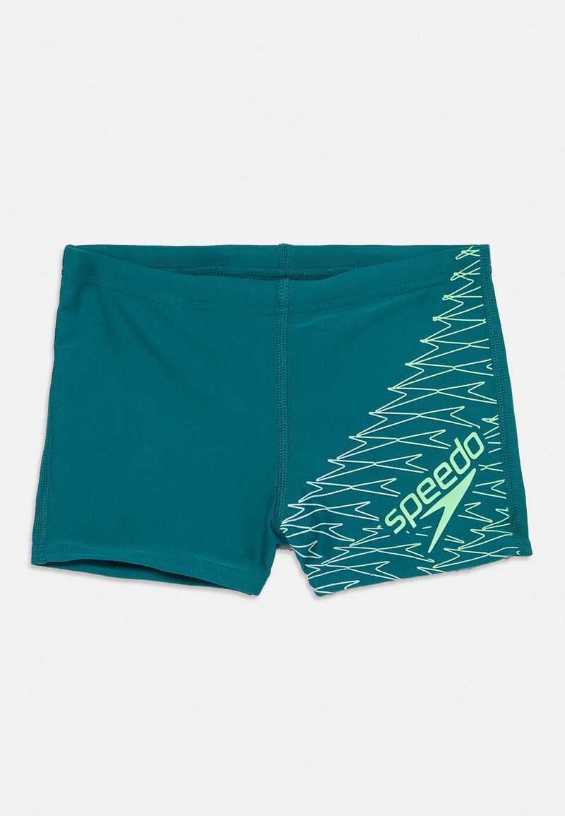 Tirkīza vīriešu peldbikses ar neona zilganzaļu zigzaga rakstu un Speedo logo vienā pusē, novietotas uz baltas virsmas.