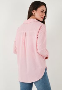 Pink and white striped shirt with a back pleat, collared neckline, and long sleeves. Soft fabric with a relaxed fit and curved hem.