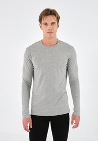Gray long-sleeve shirt made of soft fabric, featuring a round neckline and a fitted design, paired with black pants.