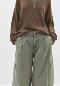 Brun textured oversized sweater parret med grønne cargo bukser med en plisseret front og sidelomme detaljer.