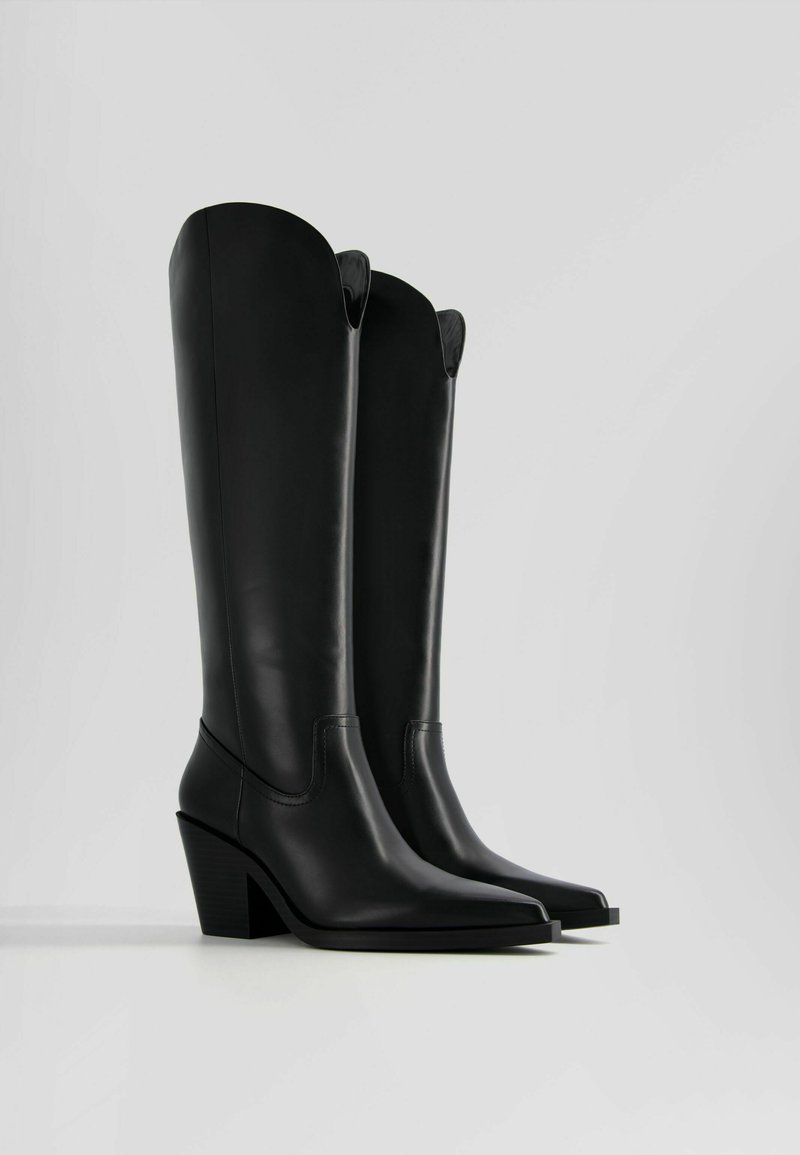 Bottes noires en cuir jusqu'au genou avec un bout pointu et un talon block sculpté. Présentent une finition lisse et un détail en haut courbé.