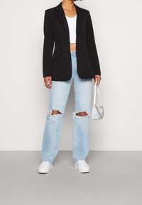 Černý blazer s klopami, kombinovaný se světle modrými džínami s efektem opotřebení. Modelka drží malou modrou kabelku a má na sobě bílé tenisky.