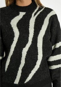 Schwarzer Strickpullover mit weißen abstrakten Streifen, Rundhalsausschnitt und strukturiertem Stoff. Das Design umfasst unterschiedlich breite Streifen.